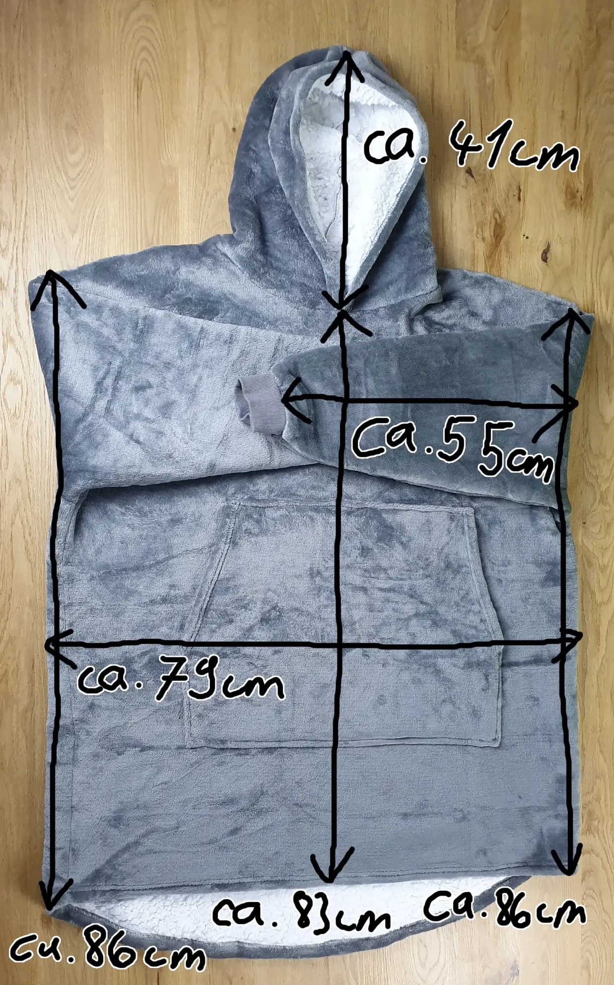 Ein Bild vom Decken-Hoodie in der Farbe Grau auf dem Tischh liegend mit den Maßen des Decken-Hoodies eingezeichnet