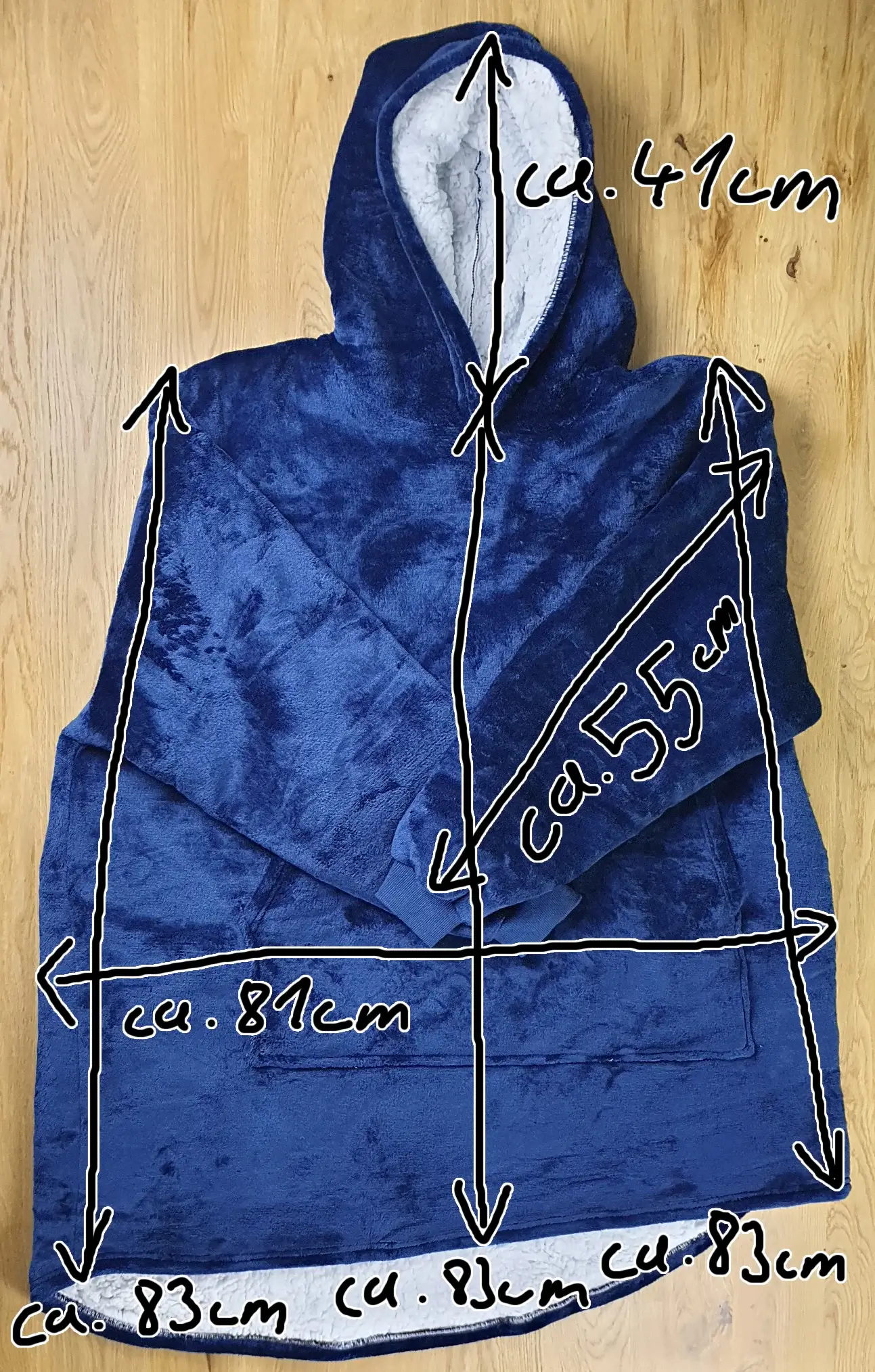 Ein Bild vom Decken-Hoodie im Blauen-Design auf dem Tischh liegend mit den Maßen des Decken-Hoodies eingezeichnet
