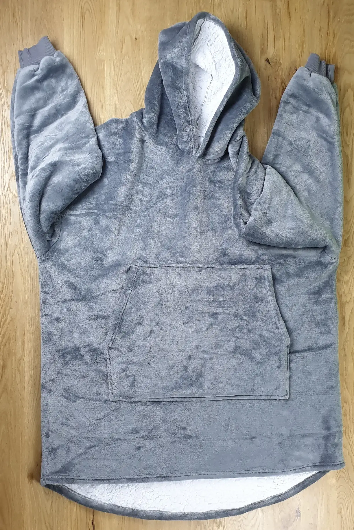 Ein Photo des Decken-Hoodies in der Farbe Grau auf den Tisch gelegt mit der Vorderseite zur Kamera. Die Ärmel sind dabei nach oben gelegt.
