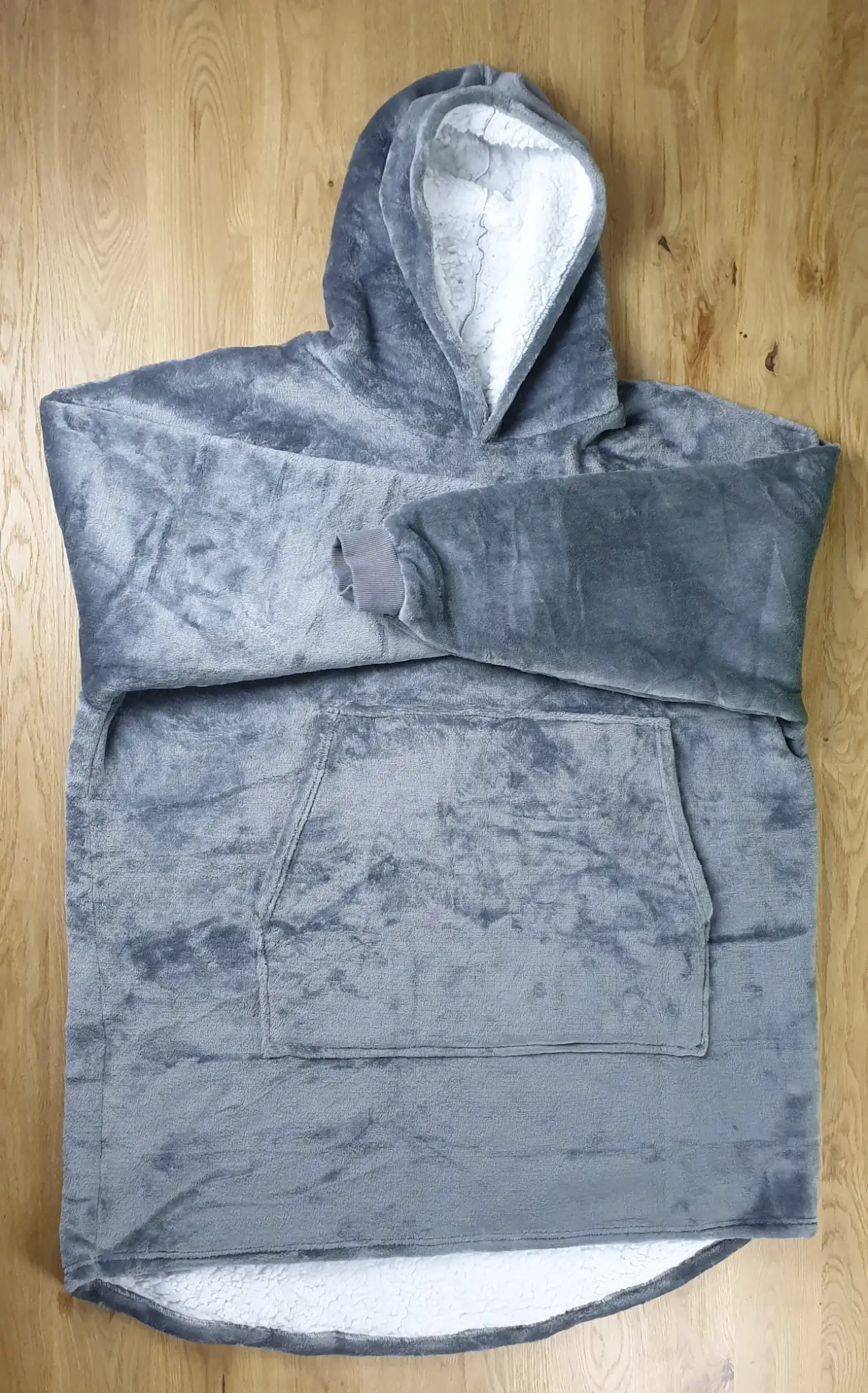 Ein Photo des Decken-Hoodies in der Farbe Grau auf den Tisch gelegt mit der Vorderseite zur Kamera. Die Ärmel sind dabei übereinander überkreuzend in der Mitte gelegt.