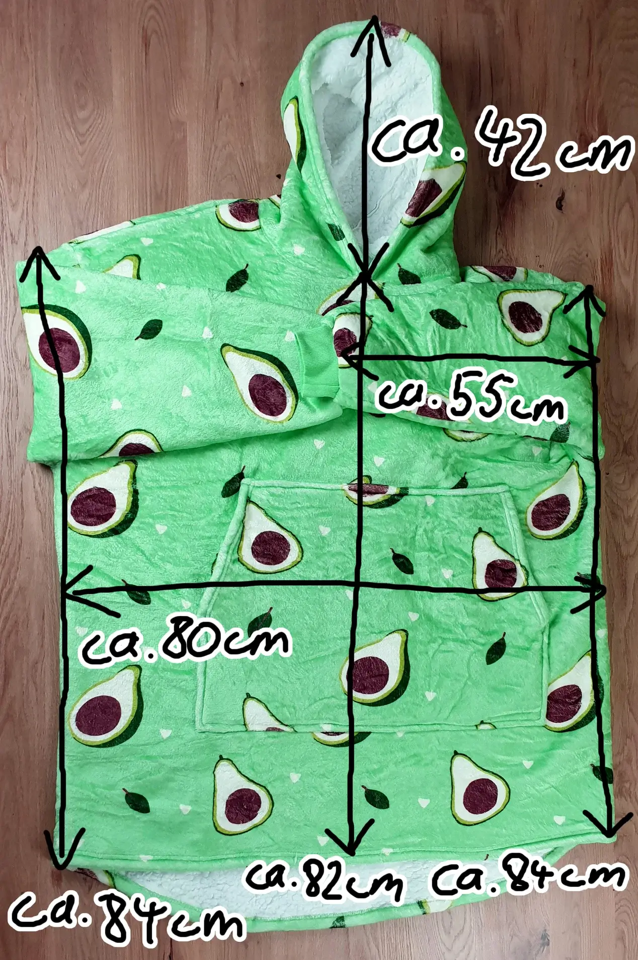 Ein Bild vom Decken-Hoodie im Avocado-Design auf dem Tischh liegend mit den Maßen des Decken-Hoodies eingezeichnet