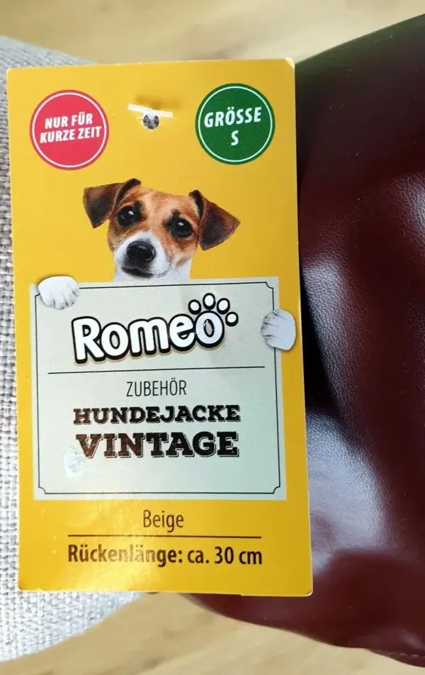 Ein Foto der Vorderseite des Etiketts der Romeo Hundejacke im Vintage-Stil in Beige mit einer Rückenlänge von etwa 30 cm.